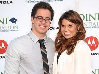 Tim Belusko is wearing a shirt, tie, and specs whereas, Danielle Fishel is wearing a white jacket.